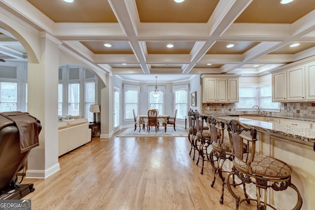 kitchen with cream cabinetry, hanging light fixtures, light stone counters, and a healthy amount of sunlight