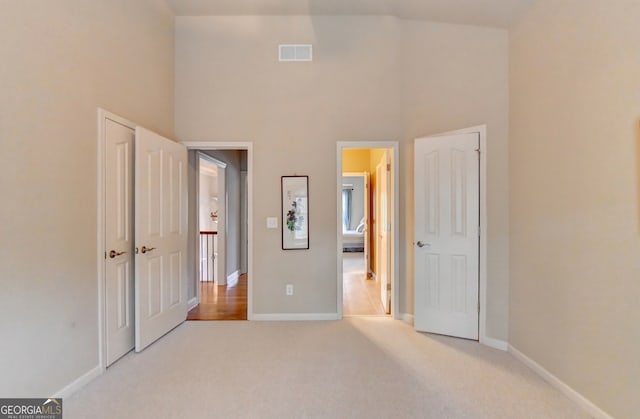 unfurnished bedroom featuring light carpet and a high ceiling