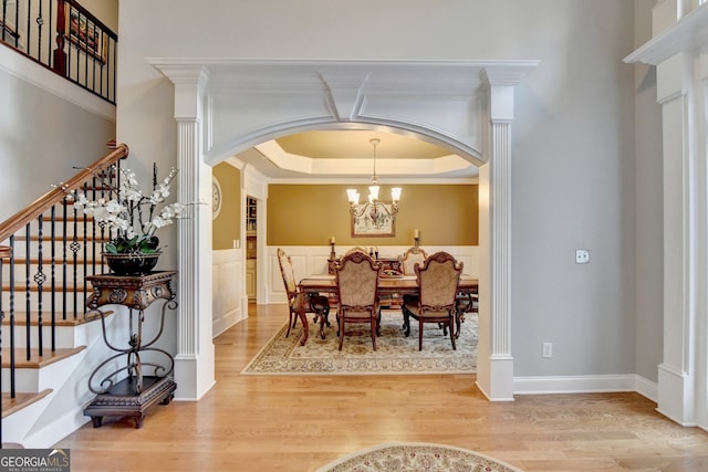 dining room featuring wood-type flooring, ornamental molding, ornate columns, a tray ceiling, and a chandelier