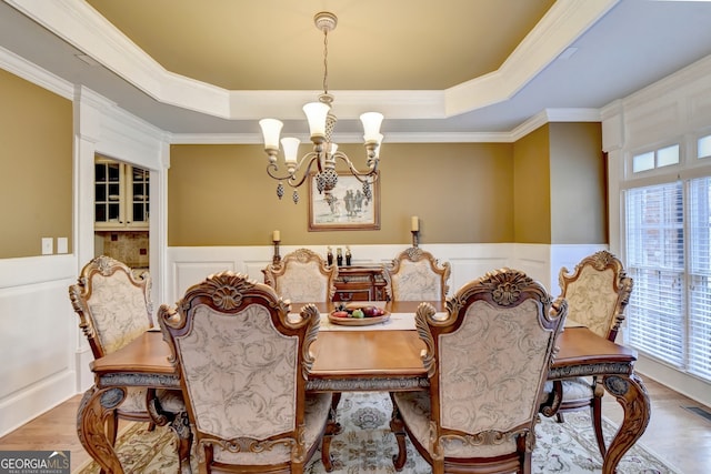 dining area with hardwood / wood-style flooring, a tray ceiling, a notable chandelier, and ornamental molding