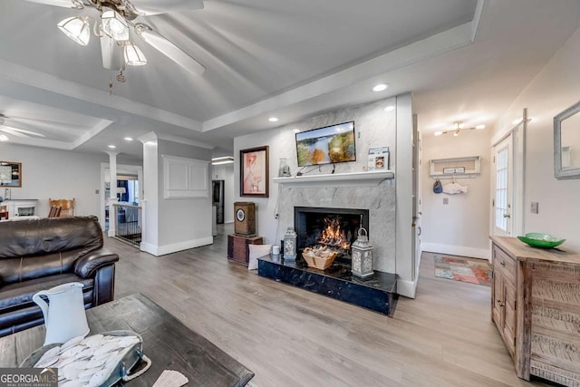 living room featuring a raised ceiling, a fireplace, ceiling fan, and light hardwood / wood-style flooring