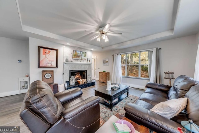 living room featuring ceiling fan, wood-type flooring, a high end fireplace, and a tray ceiling