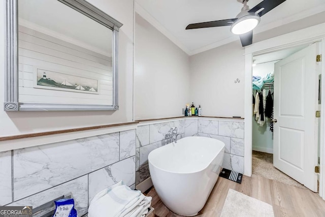 bathroom with a bathing tub, ceiling fan, crown molding, hardwood / wood-style floors, and tile walls