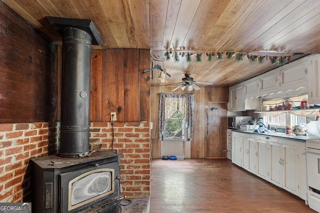 kitchen featuring stainless steel microwave, wood ceiling, white cabinets, and a wood stove