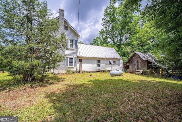 rear view of house with a yard, an outbuilding, metal roof, and a chimney