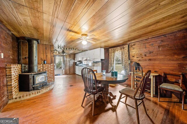 dining room with wood walls, wooden ceiling, a wood stove, wood finished floors, and a ceiling fan