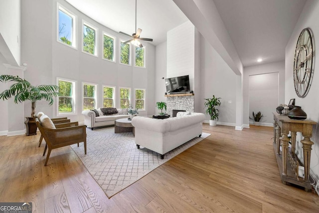 living room featuring a fireplace, light hardwood / wood-style floors, ceiling fan, and a high ceiling