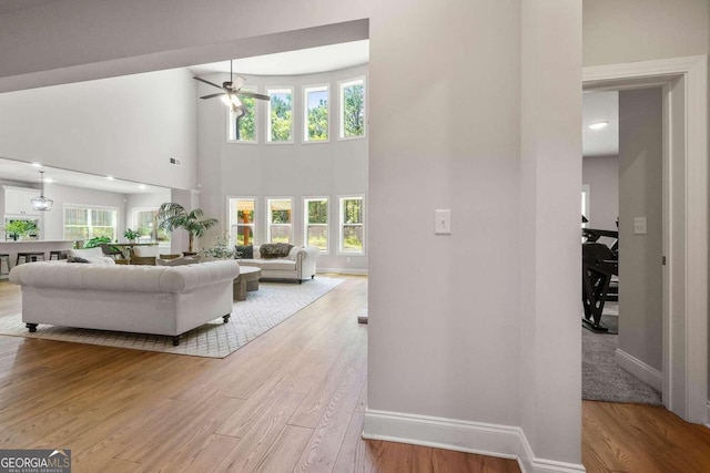 living room featuring a towering ceiling, ceiling fan, and light hardwood / wood-style flooring