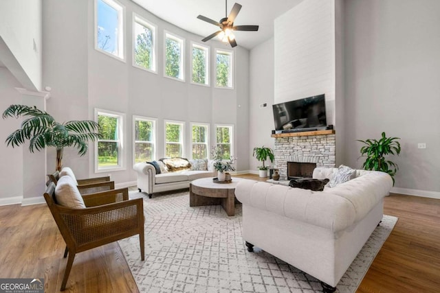 living room with a wealth of natural light, a high ceiling, a stone fireplace, and hardwood / wood-style flooring