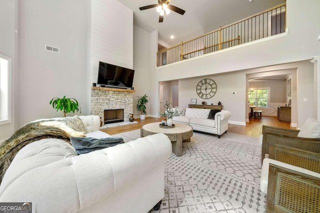 living room featuring a stone fireplace, ornate columns, hardwood / wood-style flooring, ceiling fan, and a high ceiling