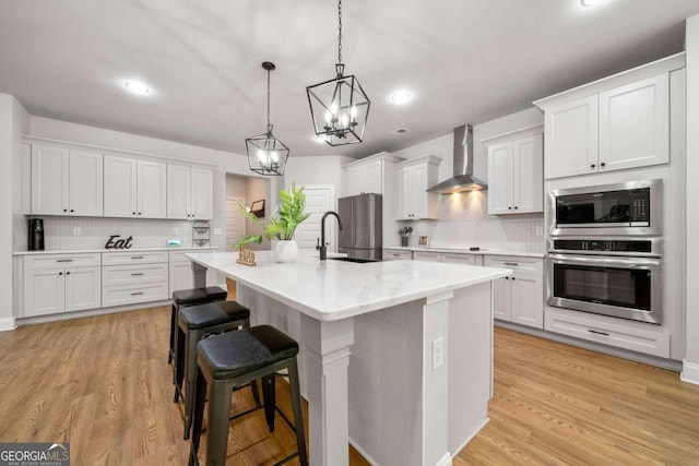 kitchen with white cabinets, wall chimney exhaust hood, stainless steel fridge, and a kitchen island with sink