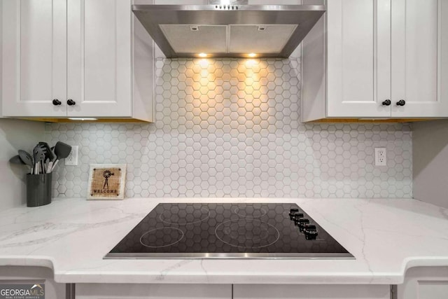 kitchen featuring black electric cooktop, wall chimney range hood, white cabinetry, and tasteful backsplash