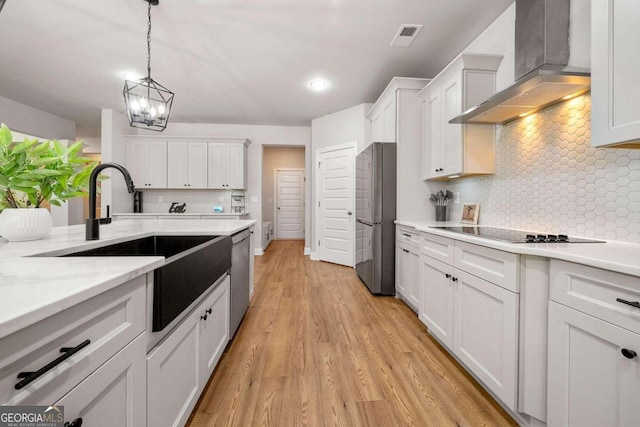 kitchen with white cabinets, appliances with stainless steel finishes, wall chimney range hood, and light hardwood / wood-style flooring