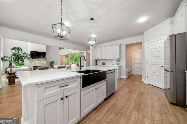 kitchen with appliances with stainless steel finishes, sink, light hardwood / wood-style floors, white cabinets, and a kitchen island with sink