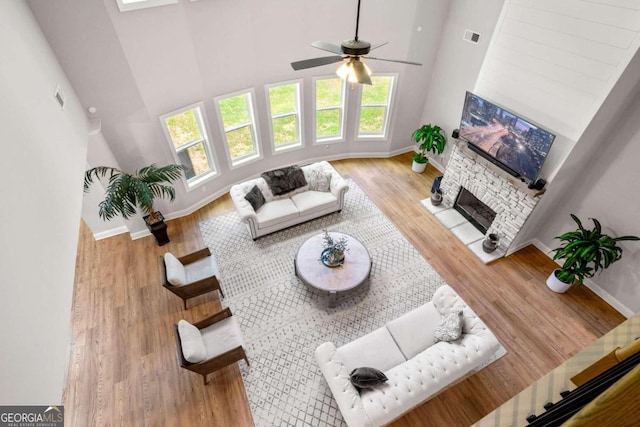 living room with a stone fireplace, hardwood / wood-style floors, ceiling fan, and a towering ceiling