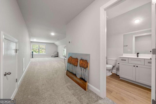 bedroom with ensuite bathroom, lofted ceiling, light carpet, and sink