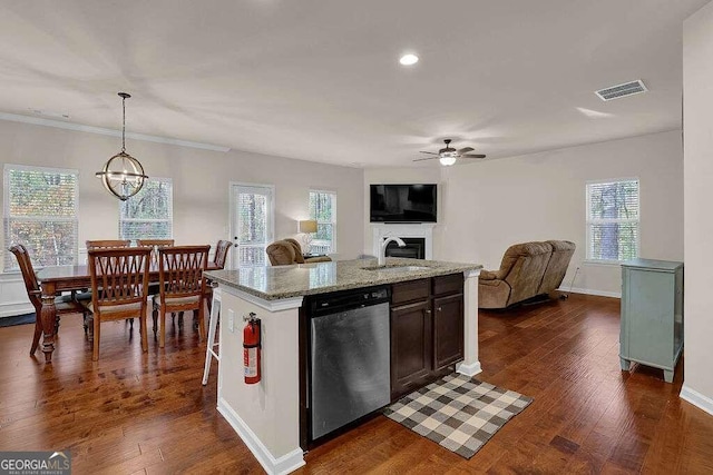 kitchen with a center island with sink, hanging light fixtures, stainless steel dishwasher, open floor plan, and light stone countertops