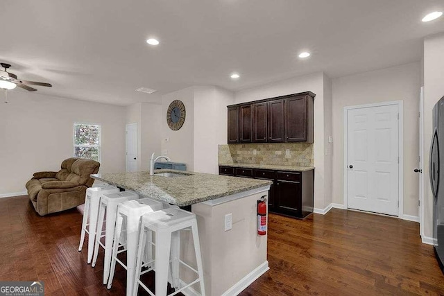 kitchen with tasteful backsplash, light stone counters, open floor plan, a kitchen island with sink, and a sink