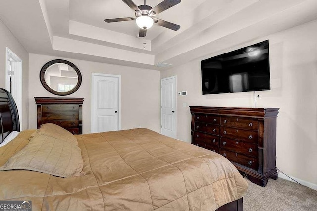 bedroom with a tray ceiling, a ceiling fan, and light colored carpet