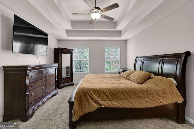 bedroom with light carpet, baseboards, a tray ceiling, and ceiling fan