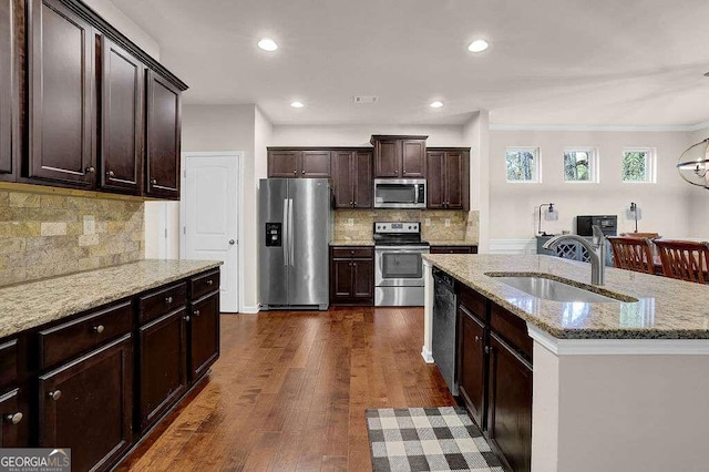 kitchen with dark wood-style flooring, appliances with stainless steel finishes, a sink, an island with sink, and dark brown cabinets