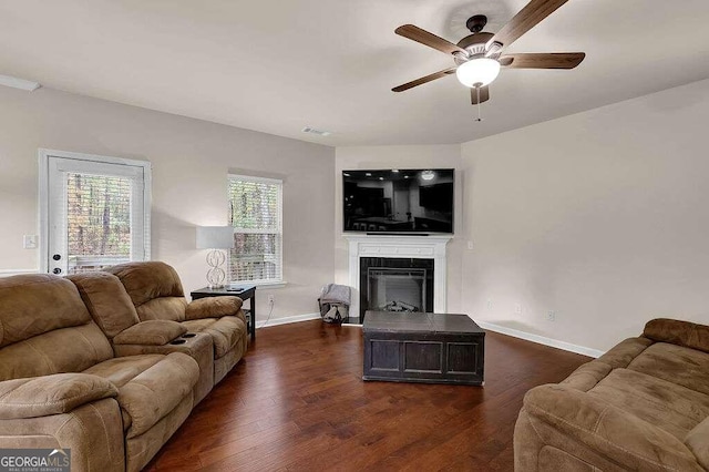 living area featuring dark wood-type flooring, a fireplace, a ceiling fan, and baseboards