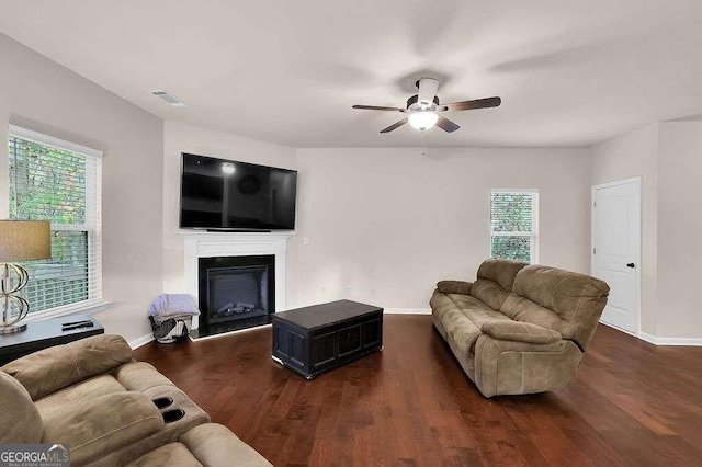 living area with a fireplace with raised hearth, baseboards, dark wood finished floors, and a ceiling fan