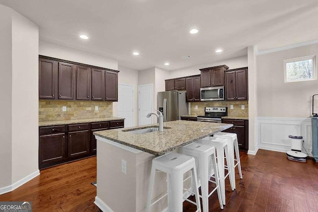 kitchen with stainless steel appliances, dark hardwood / wood-style flooring, light stone countertops, sink, and a kitchen island with sink