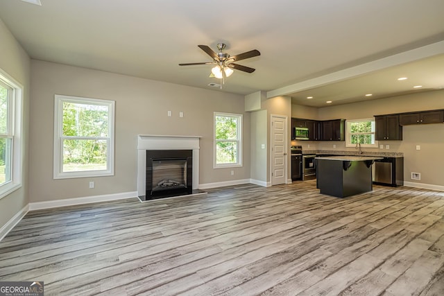 kitchen with a breakfast bar area, dark brown cabinets, stainless steel appliances, a kitchen island, and light wood-type flooring