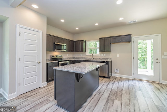 kitchen with sink, light stone counters, a center island, light wood-type flooring, and appliances with stainless steel finishes