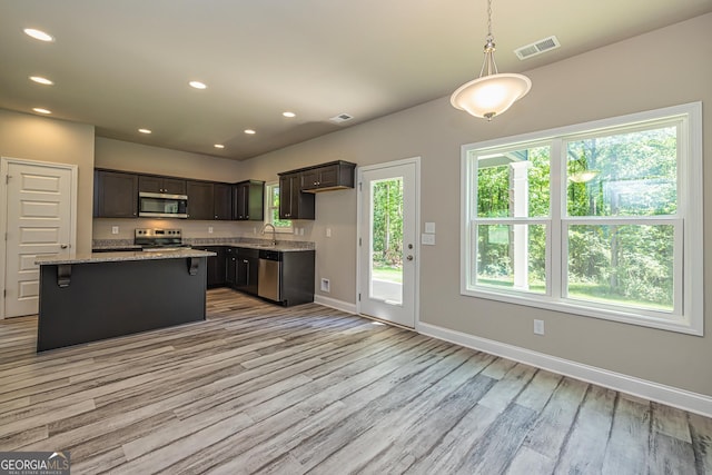 kitchen featuring dark brown cabinetry, light stone counters, appliances with stainless steel finishes, a kitchen island, and pendant lighting