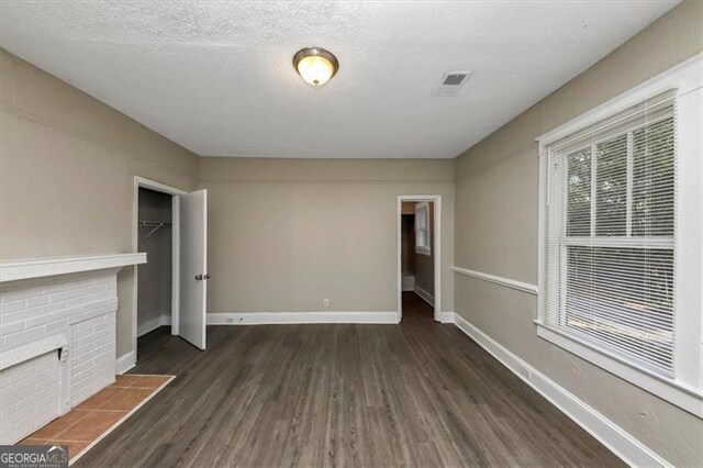 unfurnished living room with a fireplace, dark wood-type flooring, and a textured ceiling