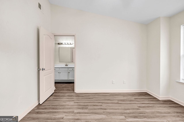 unfurnished bedroom featuring light hardwood / wood-style flooring, lofted ceiling, sink, and connected bathroom