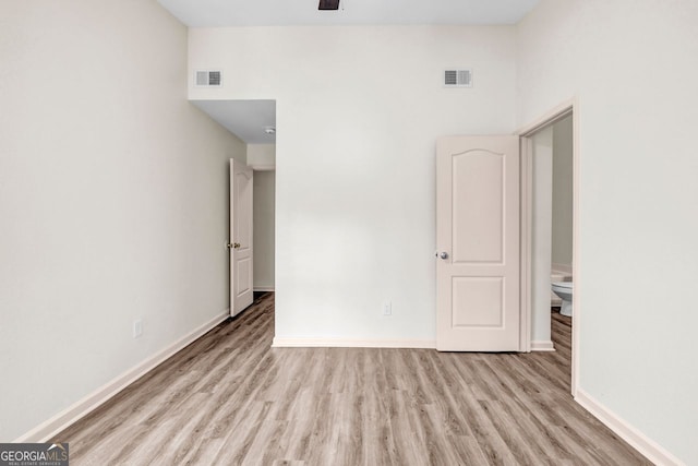 unfurnished bedroom featuring a towering ceiling, ensuite bath, and light wood-type flooring