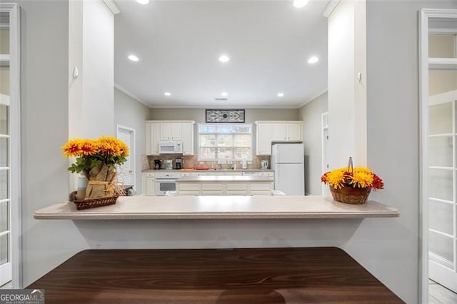 kitchen featuring kitchen peninsula, a kitchen breakfast bar, tasteful backsplash, white appliances, and white cabinets