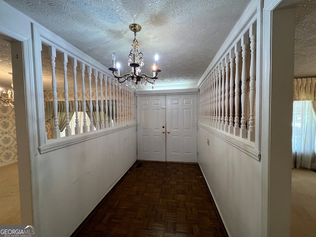 corridor featuring dark parquet floors, an inviting chandelier, and a textured ceiling