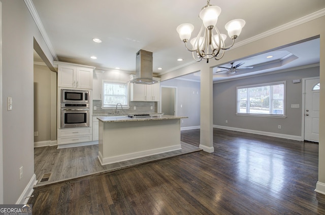 kitchen featuring island exhaust hood, ceiling fan with notable chandelier, stainless steel appliances, decorative light fixtures, and white cabinetry