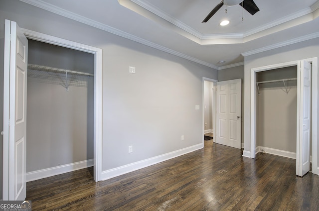 unfurnished bedroom featuring ceiling fan, dark wood-type flooring, crown molding, a tray ceiling, and two closets