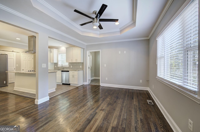 unfurnished living room with ceiling fan, sink, dark wood-type flooring, a raised ceiling, and ornamental molding