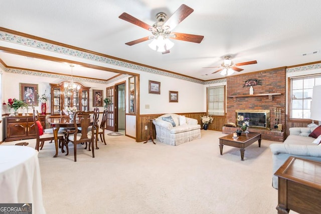 carpeted living room with ornamental molding, ceiling fan with notable chandelier, a fireplace, and wooden walls