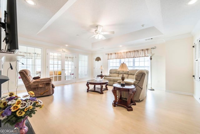 living room with ceiling fan, french doors, light hardwood / wood-style floors, and a raised ceiling