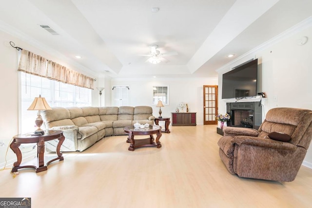 living room featuring light hardwood / wood-style floors, ornamental molding, a tray ceiling, and ceiling fan