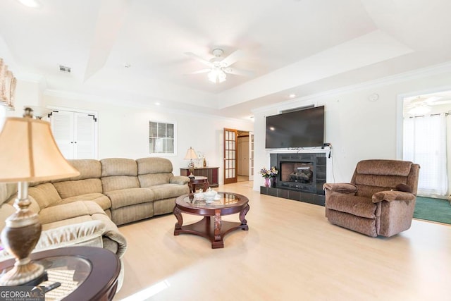 living room featuring ceiling fan, a tile fireplace, light wood-type flooring, and a tray ceiling