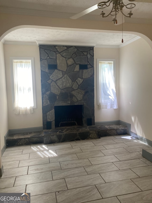 unfurnished living room with crown molding, a stone fireplace, a textured ceiling, light hardwood / wood-style floors, and ceiling fan