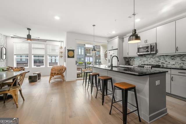 kitchen with stainless steel appliances, light hardwood / wood-style flooring, hanging light fixtures, and a center island with sink