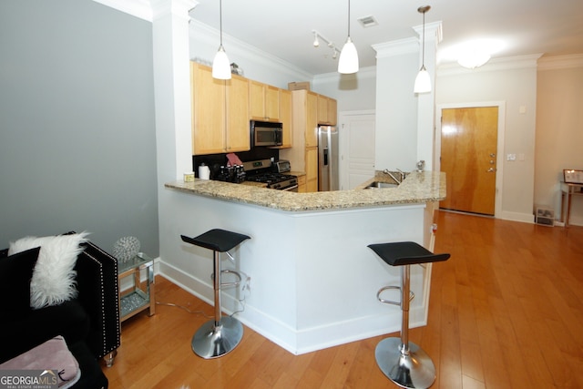 kitchen featuring kitchen peninsula, appliances with stainless steel finishes, light brown cabinetry, decorative light fixtures, and light wood-type flooring