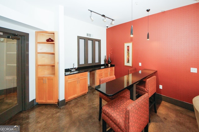 kitchen with track lighting, light brown cabinetry, pendant lighting, sink, and a breakfast bar