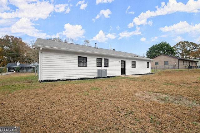 rear view of house with central air condition unit and a lawn