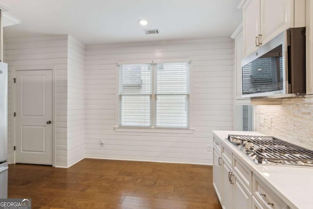 kitchen featuring dark hardwood / wood-style floors, stainless steel appliances, white cabinets, wooden walls, and decorative backsplash