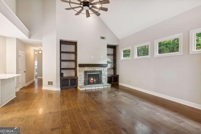 unfurnished living room featuring a stone fireplace, ceiling fan, hardwood / wood-style floors, and high vaulted ceiling